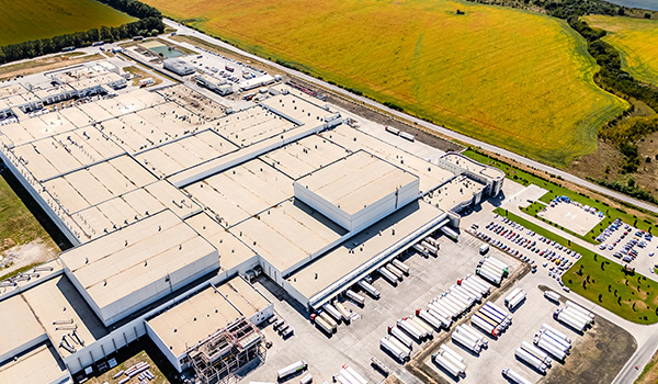 aerial view of a large industrial facility with numerous trucks parked outside and grassy fields surrounding the area emphasizing logistics and production capabilities for businesses with a focus on four expansion zones
